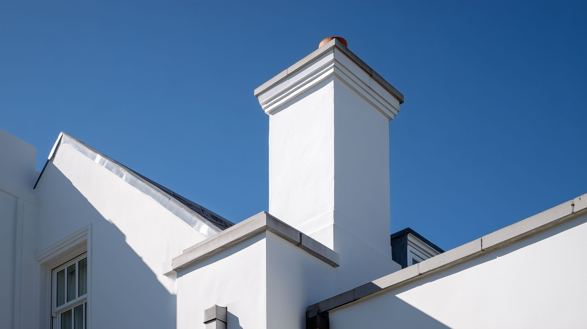 Close-up of clean white chimney and roof finish using pebblecrete over existing concrete for a smooth exterior look.