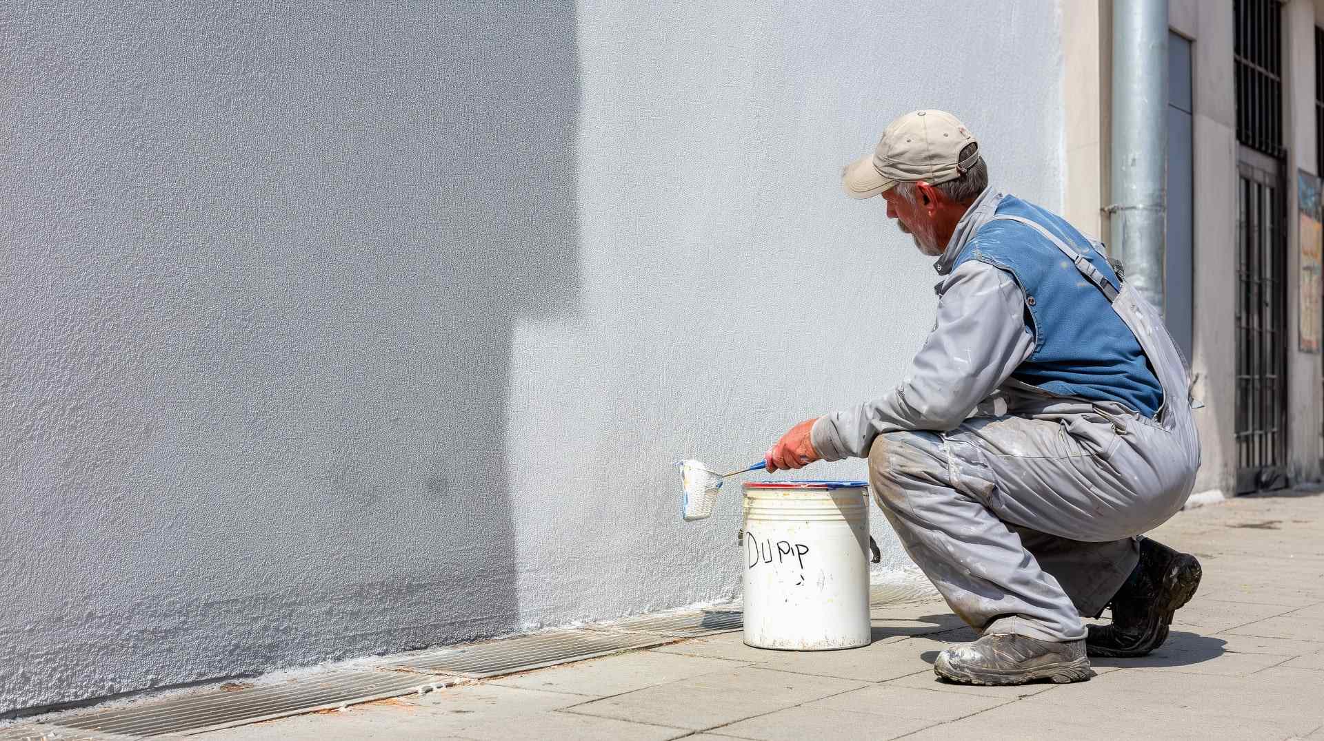 Worker applying white texture paint on exterior wall for smooth, durable surface finish.
