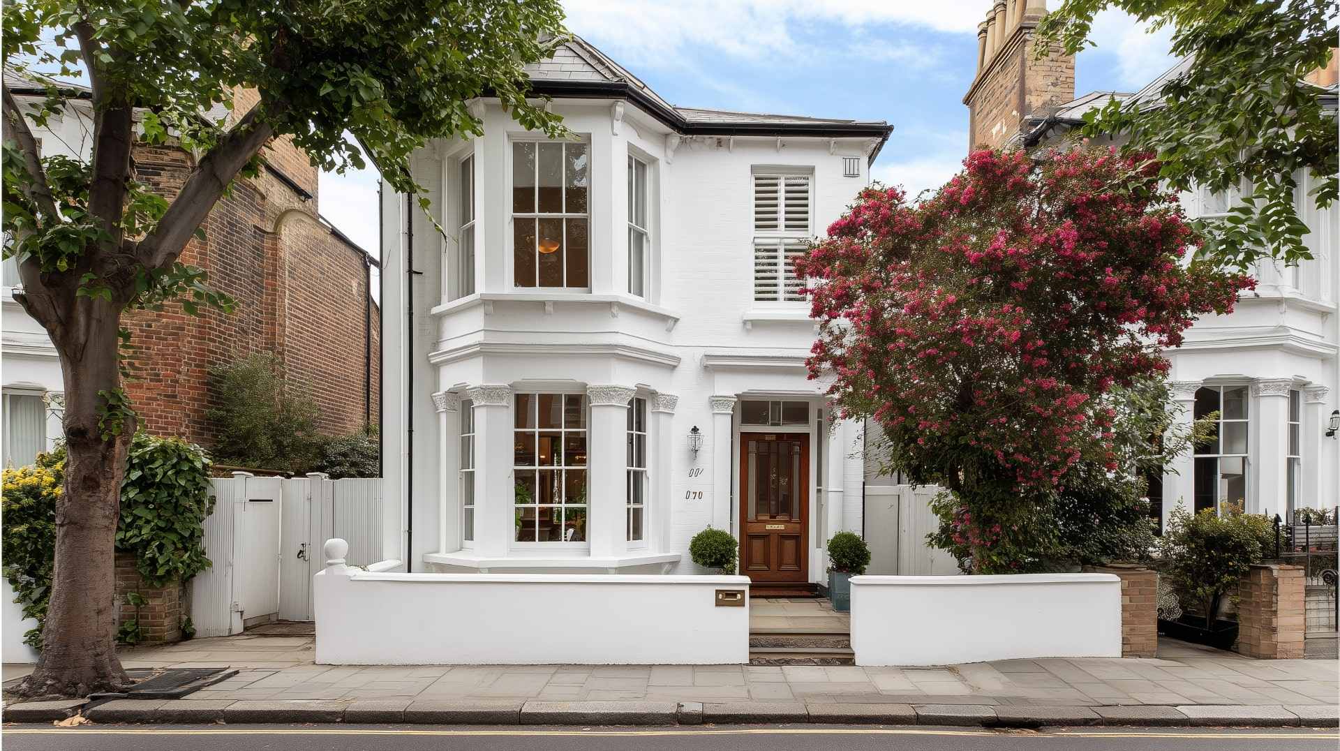 Beautiful white Victorian House with bay windows, brown door, and blooming front garden.